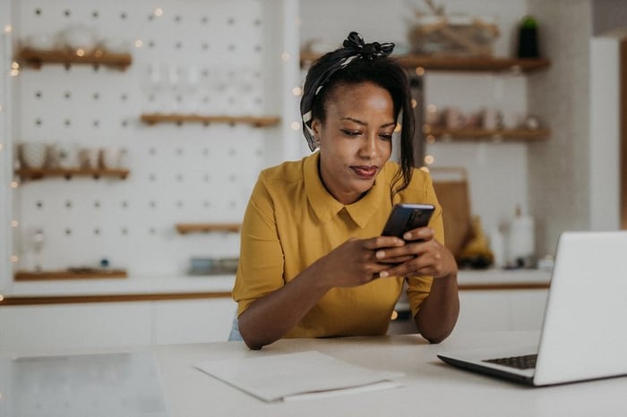 An adult with a neutral expression uses their smartphone in their kitchen.