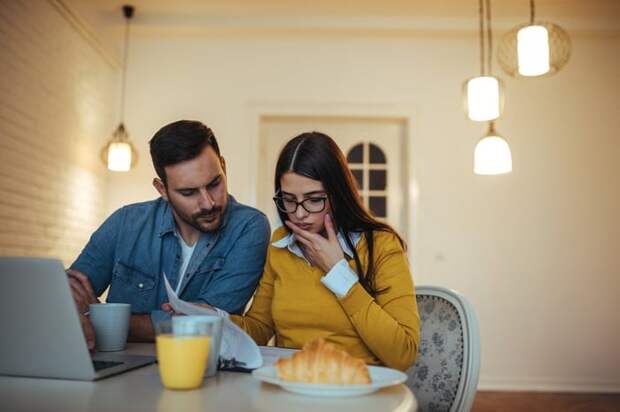 Couple eating breakfast looking at papers and laptop confused.