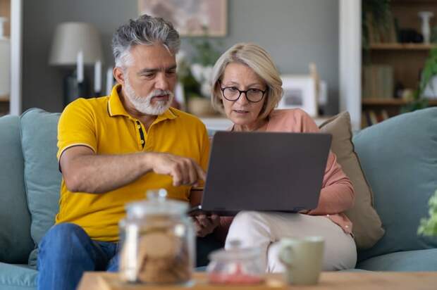 Couple sitting on a sofa, studying the screen of a laptop computer.