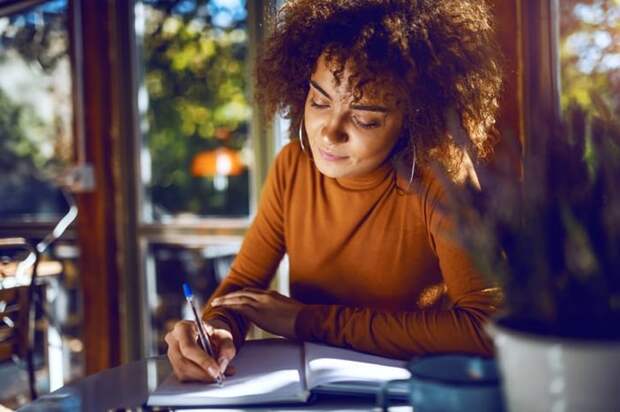 A woman sitting at a sunny table and writing in a notebook.