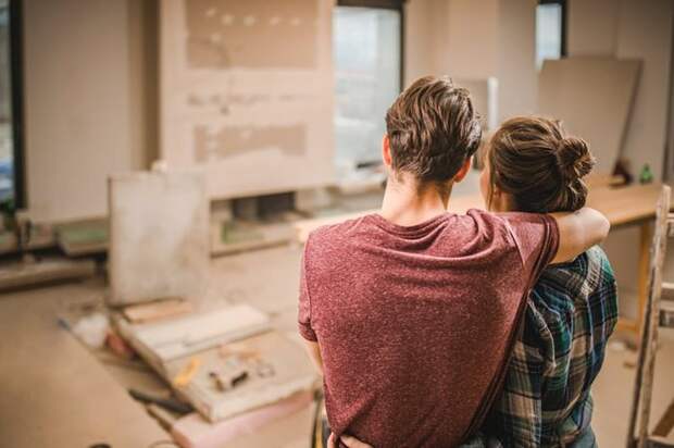 Two people with their arms around each other looking at their living room under construction.