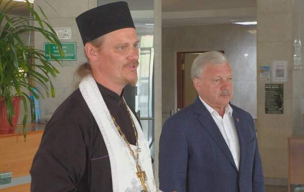 Православный священник и мужчина в костюме в здании.
