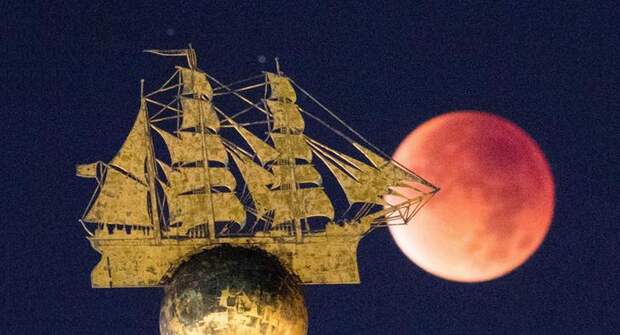 Вот как раз кровавая Луна видна над скульптурой парусника в Гамбурге, Германия