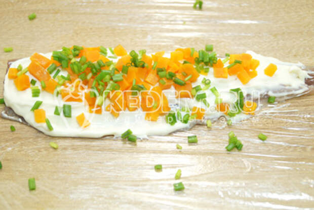 Одно из филе выложить на пищевую пленку и смазать плавленным сыром. Добавить сверху мелко нашинкованную отварную морковь и нашинкованный зеленый лук.