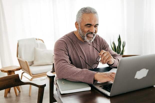 Smiling person typing on laptop and holding glasses.