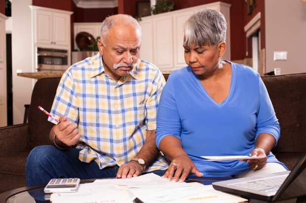 A couple seated on a couch who are examining bills and financial statements on a table in front of them.