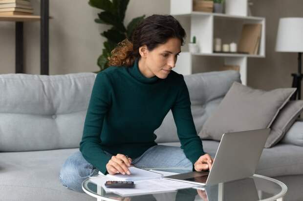 A person on a couch with a laptop and documents in front of them.