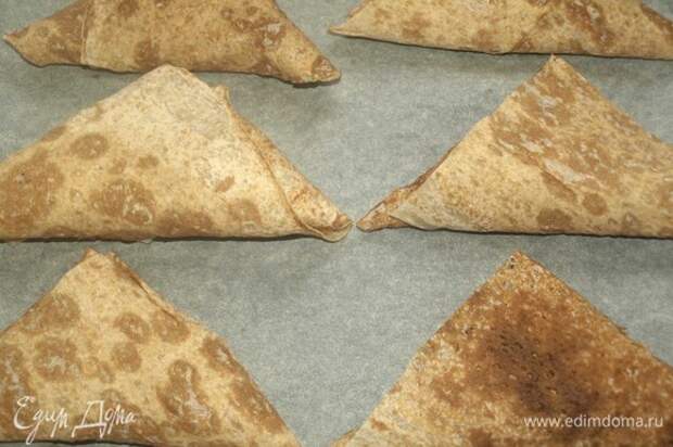 На застеленный пекарской бумагой противень кладем треугольники из лаваша. Отправляем в заранее разогретую до 180°C духовку на 7–10 минут.