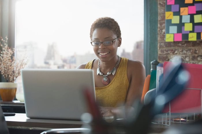 Woman smiling as she uses her laptop.