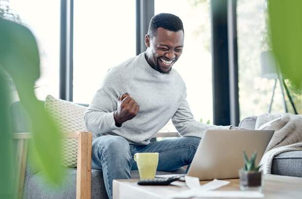 Person on couch looking at computer and cheering. 