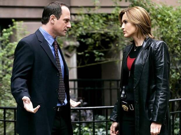 Benson and Stabler stareat each other in front of a building with plants.