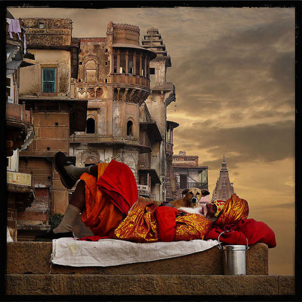 Аскет-садху, спящий на заходе солнца на фоне города Варанаси.