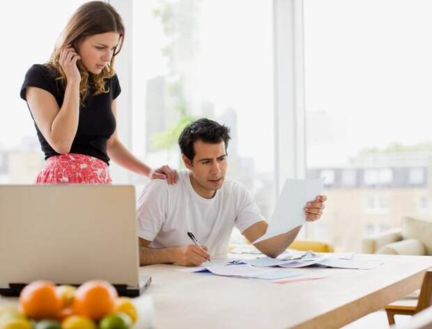 Two people looking worried while reviewing bills at their kitchen table.