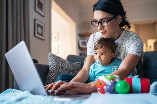 Person with baby on lap, typing on laptop.