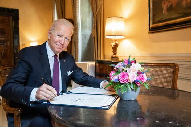 President Joe Biden holding a pen over a document.