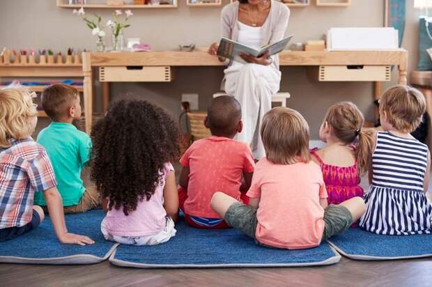 A group of children sitting on mats in a child care center listening to a story.