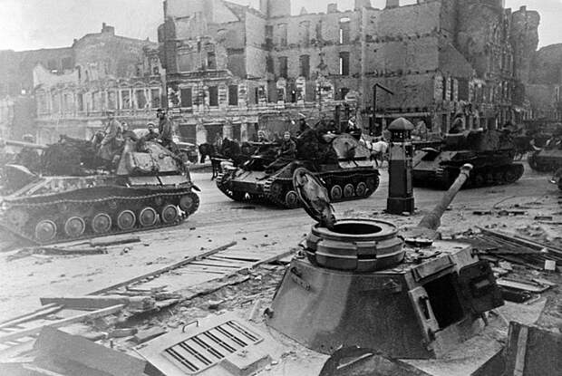 Колонна советских самоходок СУ-76 проезжает мимо закопанного немецкого танка Pz.Kpfw.IV, использовавшегося как ДОТ на улице Берлина Великая Отечественная Война, СССР, военная техника, германия