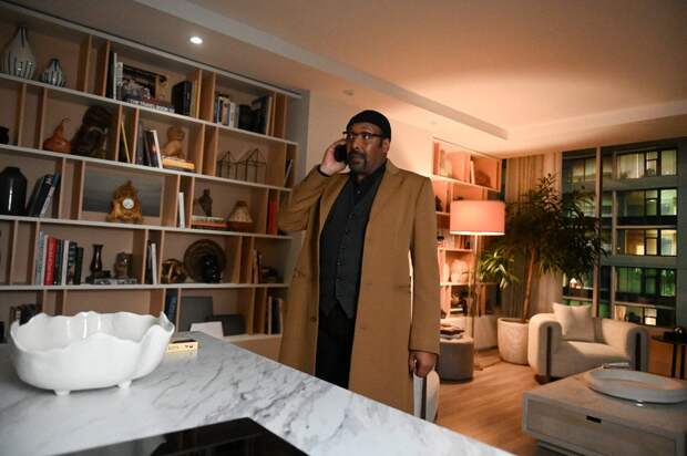 Alec on the phone in a fancy apartment next to a bookshelf on The Irrational Season 2 Episode 1