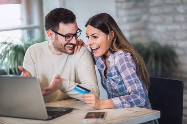 Happy couple with laptop holding a credit card and gesturing toward the screen.