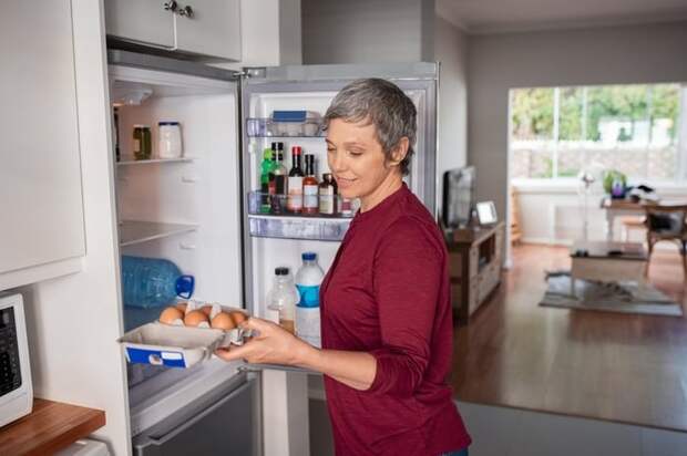 A woman opening the refrigerator and pulling out eggs.