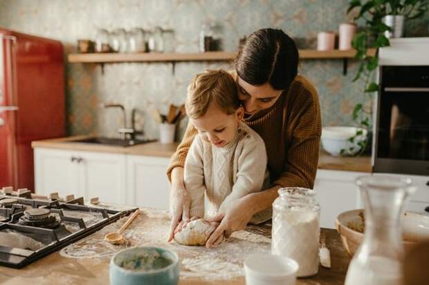 A mom and her toddler son rolling out dough on a kitchen counter.