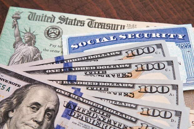 A stack of $100 bills, a Social Security card, and a U.S. Treasury check sitting atop a table.