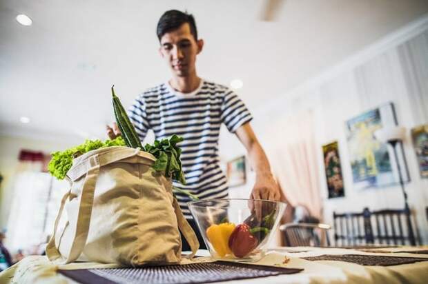 A person unpacking fruits from a grocery bag into a bowl on the dining room table.