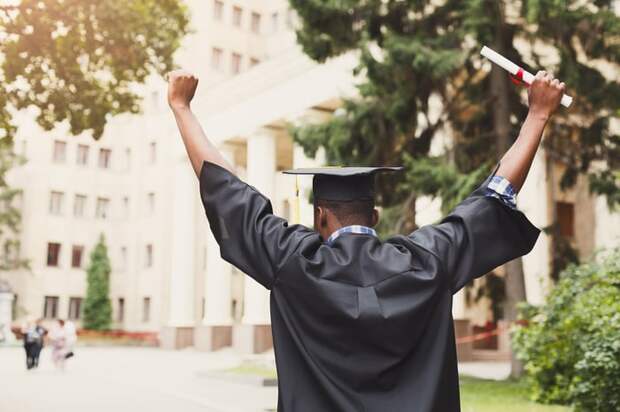 Person wearing college graduation gown with arms over head.