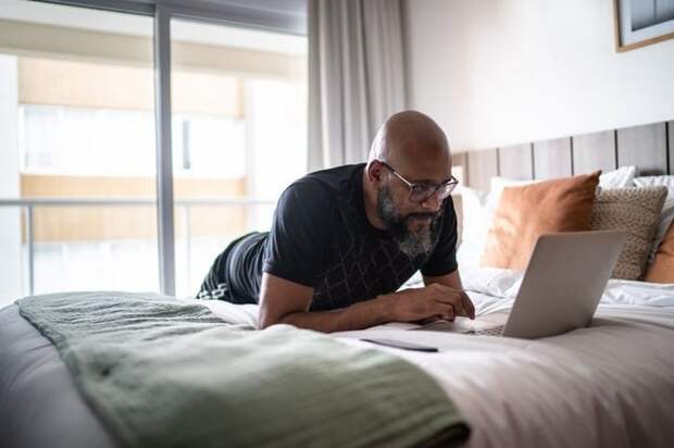 A person lying on a bed while searching on a laptop.