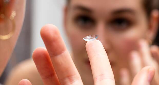a photo of a young woman putting in a contact lens, reflected in a mirror