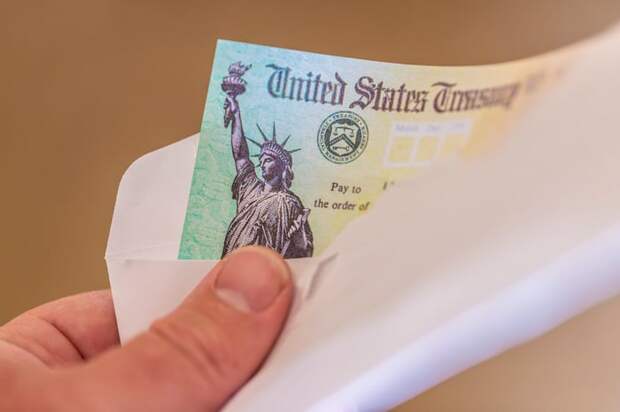 A hand holding a check from the U.S. Treasury.