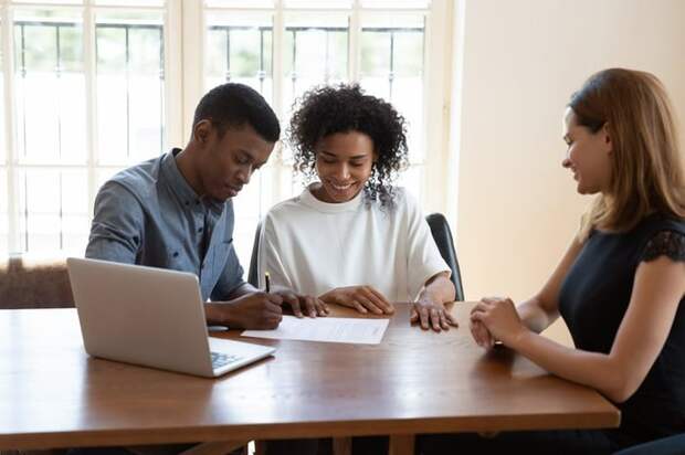 Young couple signing paperwork while a professionally dressed woman looks on.