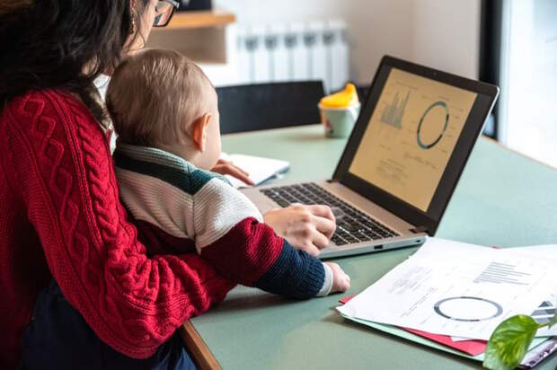 Person holds child while working on their laptop.