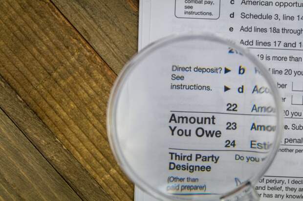 A magnifying glass held above an IRS federal tax form, enlarging the phrase Amount You Owe.