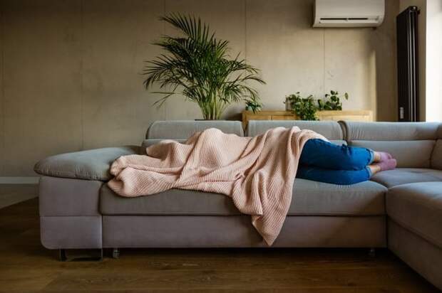 A sick person laying on their couch at home covered by a blanket.